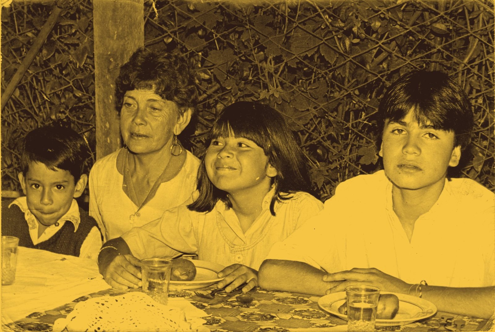 Abuela con tres niños sentados a la mesa en un patio con enredaderas, fotografía de archivo familiar