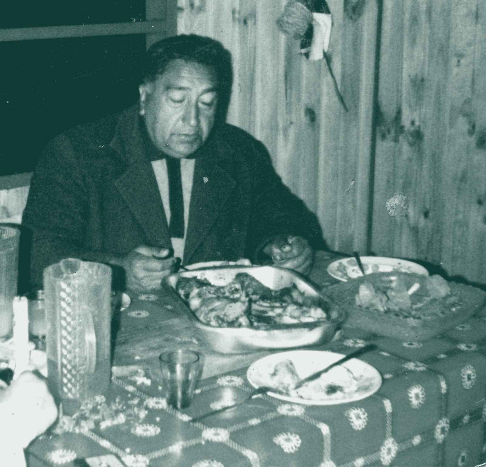 Hombre sirviéndose de una fuente en una mesa con mantel rojo, fotografía de archivo familiar